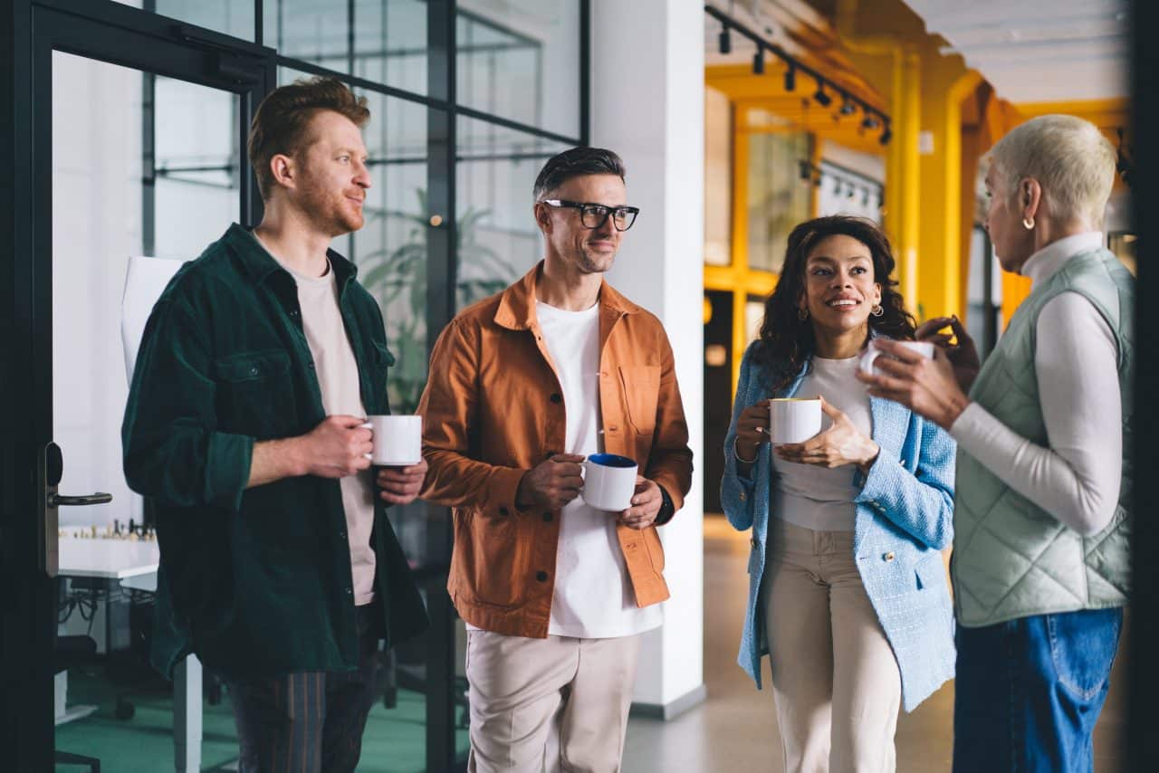 A group of male and female colleagues in business casual clothing drinking coffee while talking