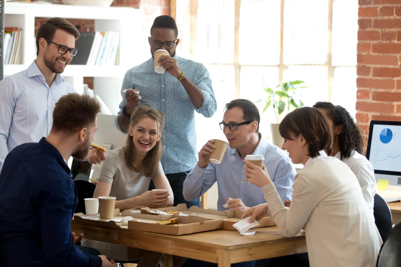 Colleagues laugh over office lunch pizza coffee