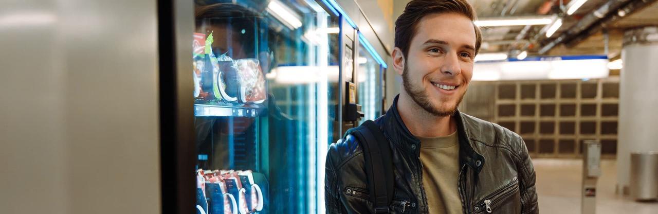 A man in a leather jacket leads against a snack vending machine