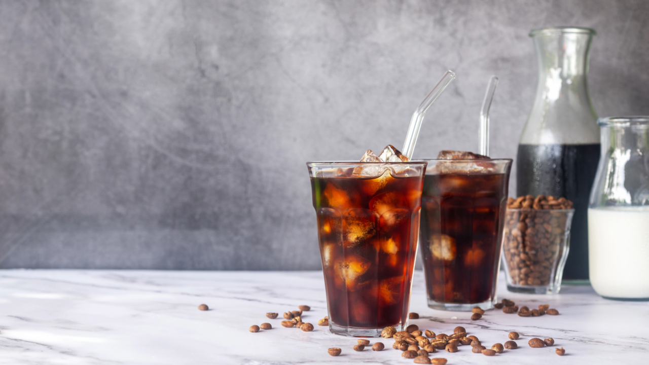 What is cold brew? Two iced coffee drinks with milk, ice cubes and a carafe of coffee in the background