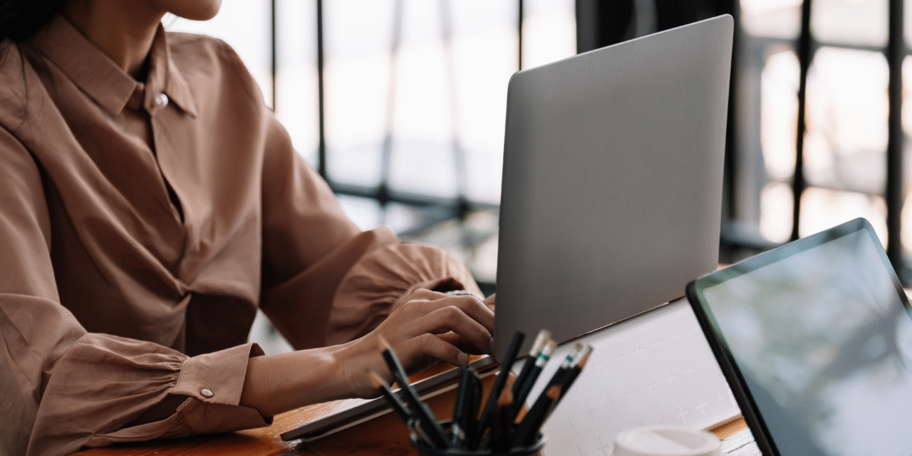 Person typing on their laptop wearing a brown satin shirt